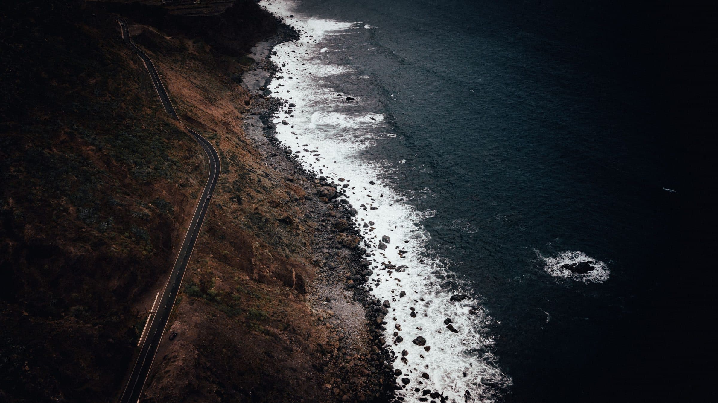 A coast road running along a dark volcanic shoreline