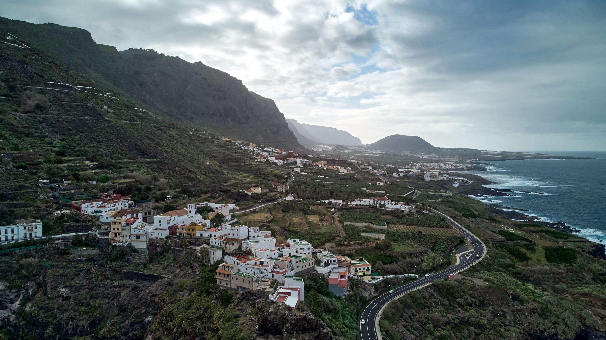 A road winding down a green hillside towards the coast
