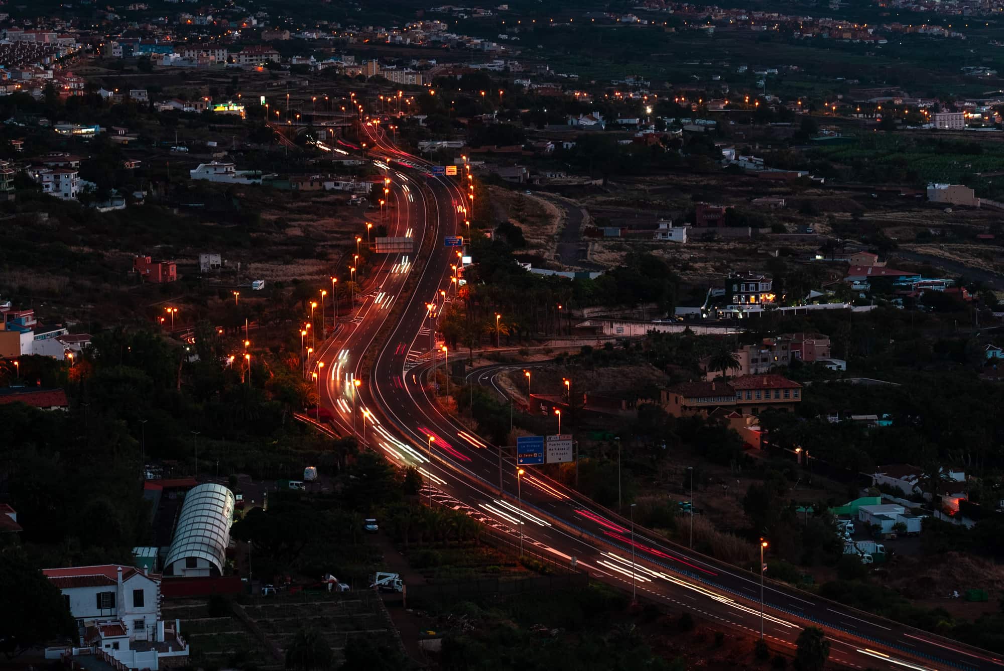 Traffic trails along a lit motorway through a valley at dusk